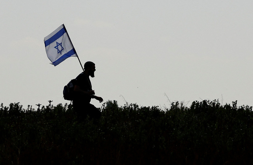  A demonstrator carries an Israeli flag as he walks through fields to avoid a check-point and reach a protest against the delivery of humanitarian aid to Gaza and demanding the immediate release of Israeli hostages kidnapped in the deadly October 7 attack, amid the ongoing conflict between Israel an (credit: SUSANA VERA/REUTERS)