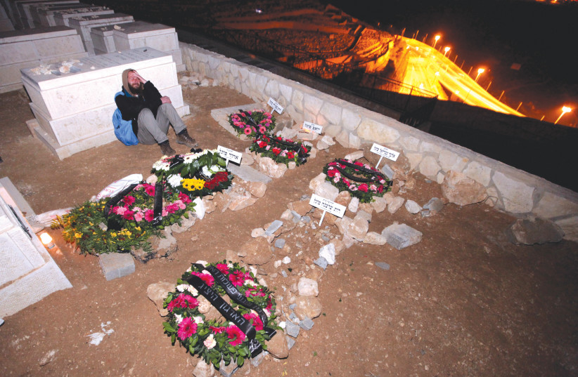  A MOURNER sits near the fresh graves of the five members of the Fogel family – mother, father, and three of their children – murdered in a Palestinian terror attack, in 2011. The White House sharply condemned the murder. But, as in the case of the October 7 events, the shock soon wore off, says the (credit: ABIR SULTAN/FLASH90)