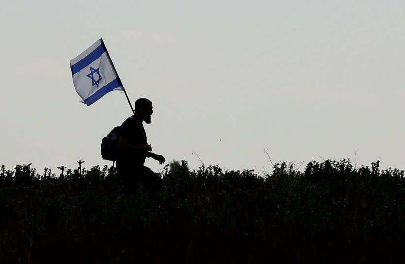  Un manifestante lleva una bandera de Israel mientras camina por campos para evitar un puesto de control y llegar a una protesta contra la entrega de ayuda humanitaria a Gaza y exigiendo la liberación inmediata de rehenes israelíes secuestrados en el mortal ataque del 7 de octubre. (credit: SUSANA VERA/REUTERS)