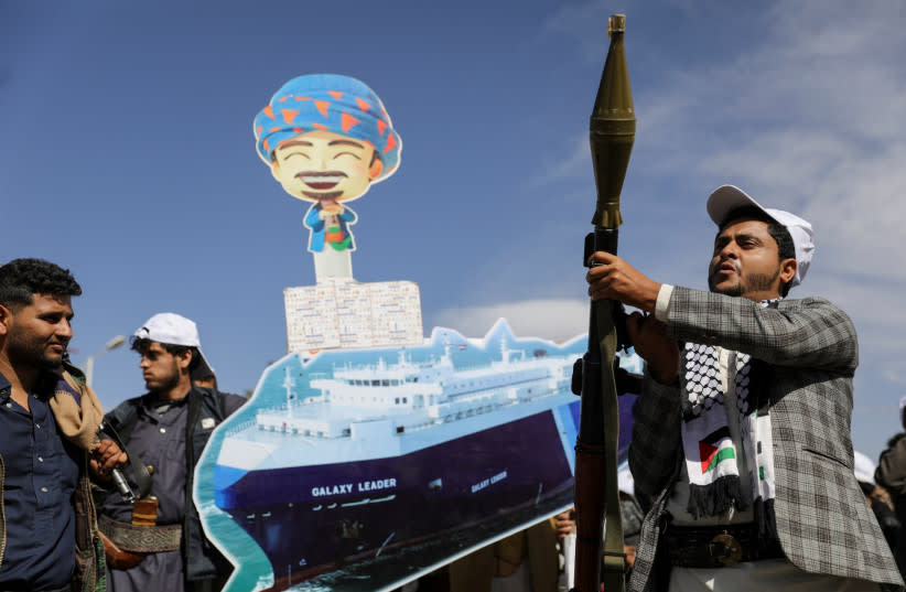 Un seguidor houthi sostiene un lanzacohetes mientras otros portan una pancarta recortada, que representa el carguero Galaxy Leader que fue tomado por los houthis, durante un desfile como parte de una campaña de movilización del ''ejército popular'' por parte del movimiento, en Saná, Yemen, 7 de febre