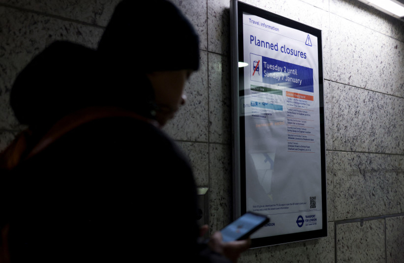 A traveler looks at a phone near an information board at Victoria station, as London Underground workers strike over pay and terms, in London, Britain, January 7, 2024 (credit: HOLLIE ADAMS/REUTERS)