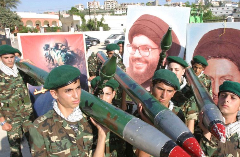  Miembros de Hezbolá portan cohetes de pega junto a un cartel del líder del grupo, Sayyed Hassan Nasralá [FIle]. (credit: REUTERS)