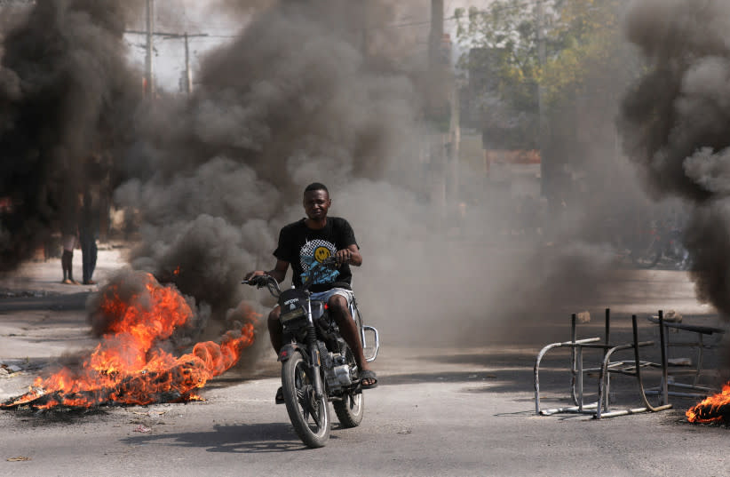  Un hombre pasa en coche junto a una barricada en llamas durante una protesta contra el gobierno del primer ministro Ariel Henry y la inseguridad, en Puerto Príncipe, Haití, 1 de marzo de 2024. (credit: REUTERS)
