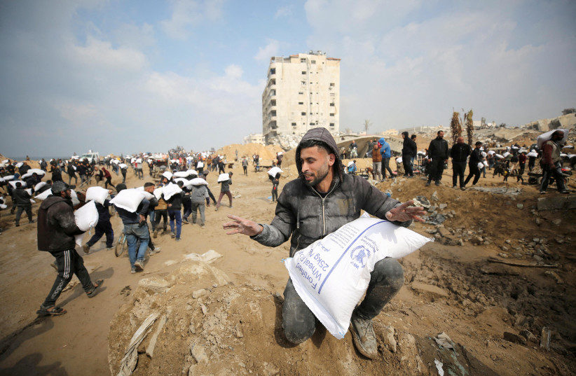  Palestinians carry bags of flour they grabbed from an aid truck near an Israeli checkpoint, as Gaza residents face crisis levels of hunger, amid the ongoing conflict between Israel and Hamas, in Gaza City, February 19, 2024.  (credit: REUTERS/Kosay Al Nemer/File Photo)