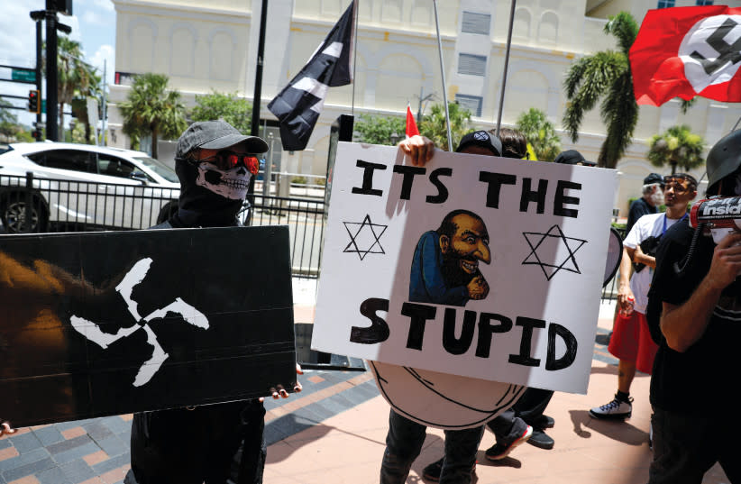  Manifestantes sostienen símbolos y carteles antisemitas mientras protestan frente al Centro de Convenciones de Tampa, donde se celebraba la Cumbre de Acción Estudiantil de Turning Point USA, en Tampa, Florida, el 23 de julio de 2022. (credit: MARCO BELLO/REUTERS)
