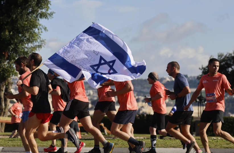 Jerusalem Marathon participants move along the race course, waving a signed Israel flag, March 8, 2024 (credit: MARC ISRAEL SELLEM/THE JERUSALEM POST)