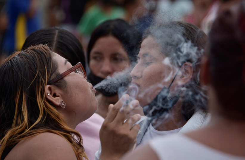  A woman blows cigarette smoke at another woman in the belief that this will help alleviate the effects of tear gas fired by police officers, during a protest to demand fair treatment of their loved ones, outside the Litoral prison in Guayaquil, Ecuador, January 22, 2024. (credit: REUTERS/VICENTE GAIBOR DEL PINO)