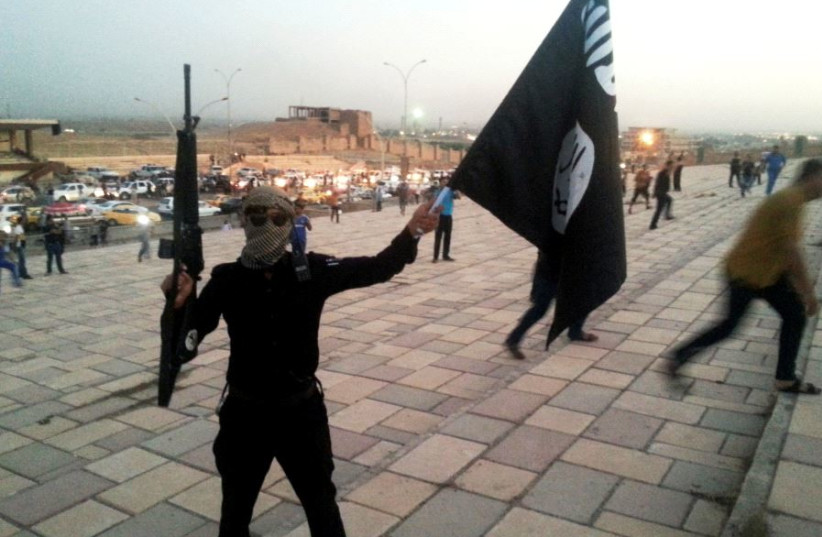  Un combatiente del Estado Islámico de Irak y el Levante (ISIL) sostiene una bandera del ISIL y un arma en una calle de la ciudad de Mosul 23 de junio de 2014. (credit: REUTERS/STRINGER)