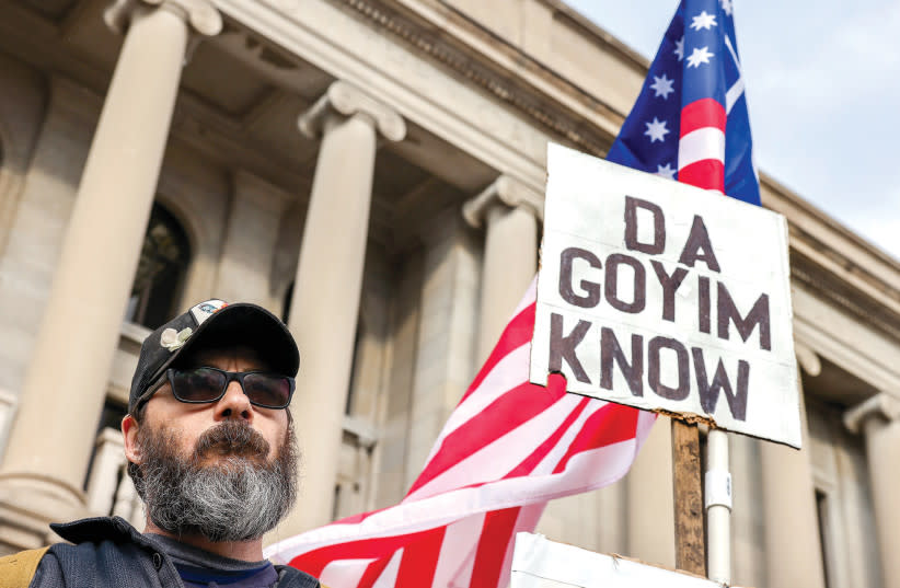 Un manifestante lleva un cartel antisemita fuera de la Corte del Condado de Kenosha durante el segundo día de deliberaciones del jurado en el juicio de Kyle Rittenhouse, en Kenosha, Wisconsin, el 17 de noviembre de 2021. (credit: EVELYN HOCKSTEIN/REUTERS)