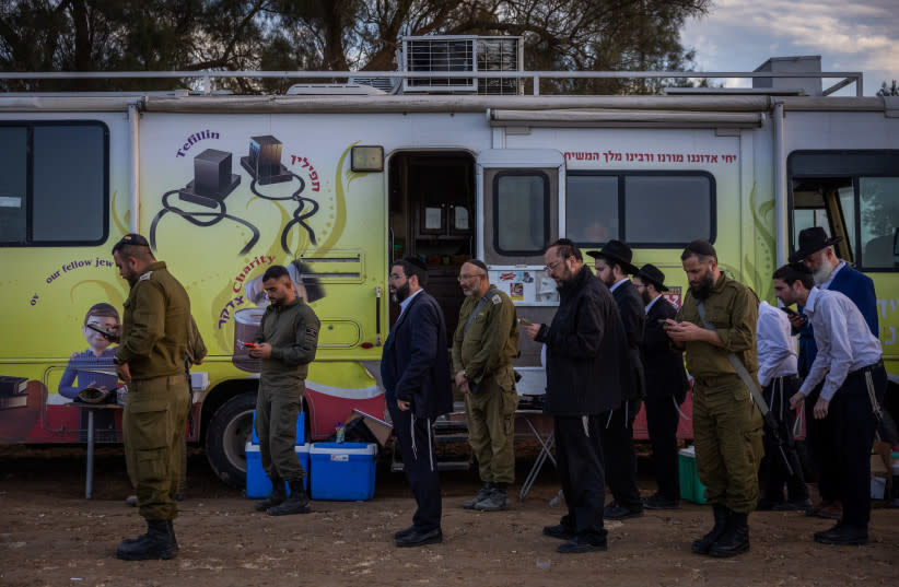 Soldados israelíes y judíos ultraortodoxos rezan en una zona de reagrupamiento cerca de la frontera entre Israel y Gaza, sur de Israel, 28 de noviembre de 2023. (credit: YONATAN SINDEL/FLASH90)
