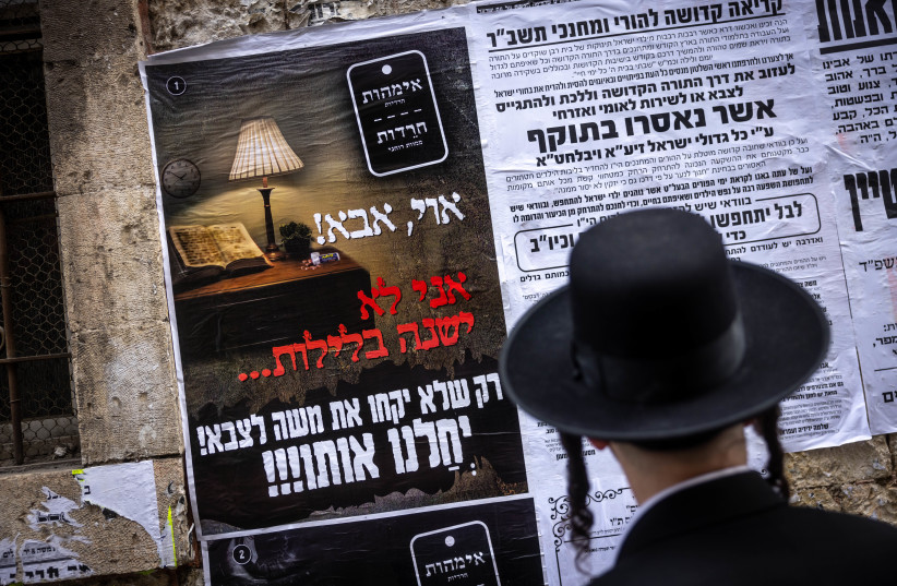 Ultra Orthodox Jews walking next to a Pashkevil on the IDF draft law in the ultra orthodox neighborhood of Mea Shearim, in Jerusalem, March 15, 2024.