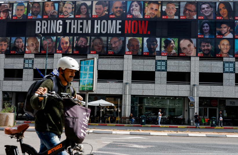  A man pushes a bike near a billboard with pictures of hostages kidnapped in the deadly October 7 attack on Israel by the Palestinian Islamist group Hamas from Gaza, in Tel Aviv, Israel March 18, 2024.  (credit: CARLOS GARCIA RAWLINS/REUTERS)