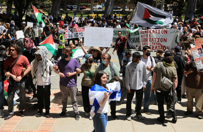 A pro-Israel counter-protester walks with an Israeli flag near protesters attending a demonstration in support of Palestinians in Gaza, amid the ongoing conflict between Israel and the Palestinian Islamist group Hamas, at the University of California Los Angeles (UCLA) in Los Angeles, California, U. (credit: DAVID SWANSON/REUTERS)
