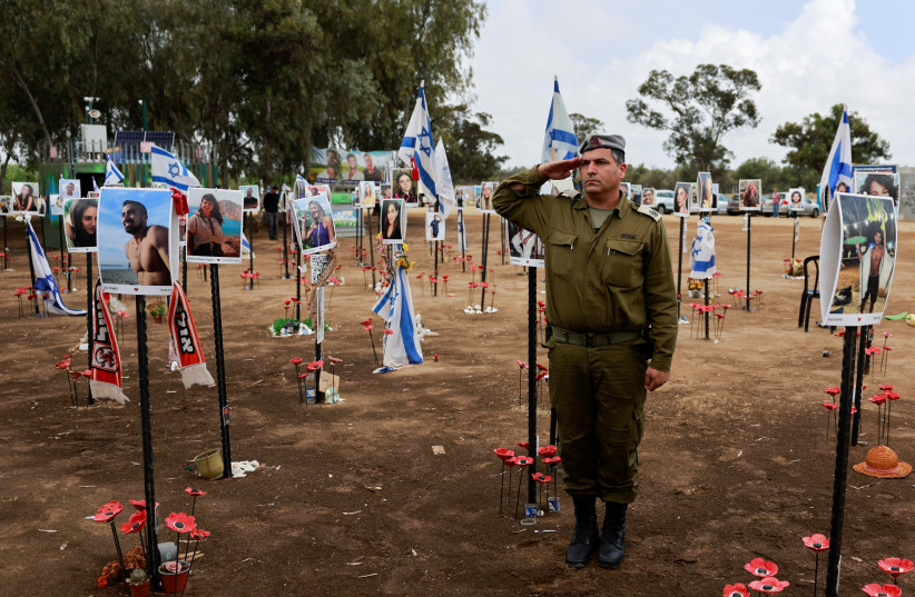 Израильский солдат стоит во время двухминутной сирены, посвященной ежегодному израильскому Дню памяти жертв Холокоста, на инсталляции на месте фестиваля Нова, где участники вечеринки были убиты и похищены во время нападения террористов ХАМАС 7 октября из сектора Газа, в Рейме, на юге страны. Израиль, 6 мая 2024 г. (Фото: AMMAR AWAD/REUTERS)