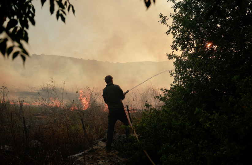  A man uses a hose to extinguish flames, in Dishon, near Kiryat Shmona, northern Israel, June 4 (credit: REUTERS/AMMAR AWAD)