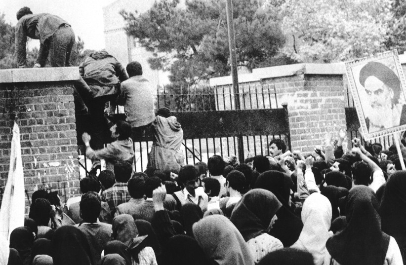 IRAN HOSTAGE crisis: Iranian students climb up US embassy gates in Tehran, November 1979. A poster of Iranian revolutionary/later supreme leader Ruhollah Khomeini is held up at R.