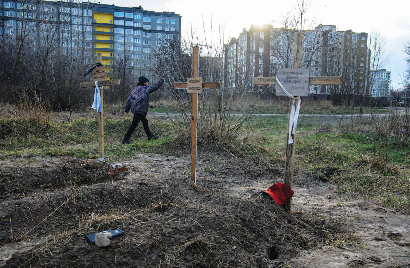  UN NIÑO camina junto a las tumbas de civiles que, según los residentes locales de Bucha, fueron asesinados por soldados rusos. La inscripción en la cruz del centro dice: ''Desconocido''.  (credit: REUTERS/VLADYSLAV MUSIIENKO)