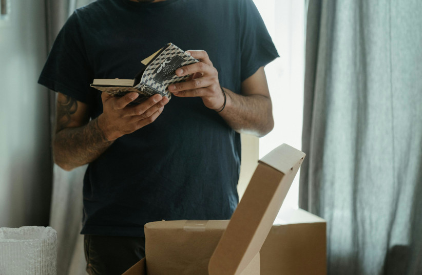 A man holds a book over a cardboard box (Illustrative) (credit: PEXELS)