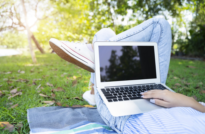  A person is seen with their laptop while laying down in the grass. (credit: INGIMAGE)