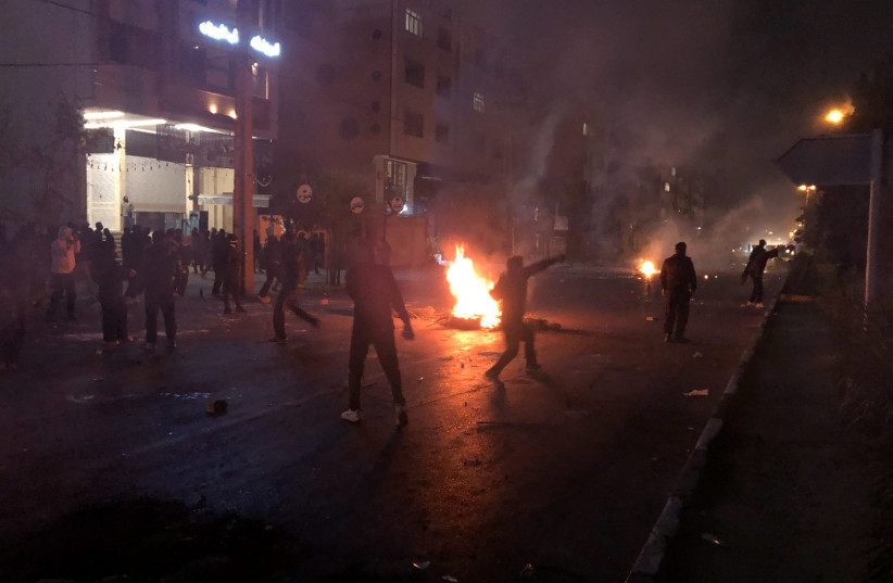A protester throws a stone near a fire as other demonstrators gather while blocking a street in Shiraz, Iran, on January 10, 2026.