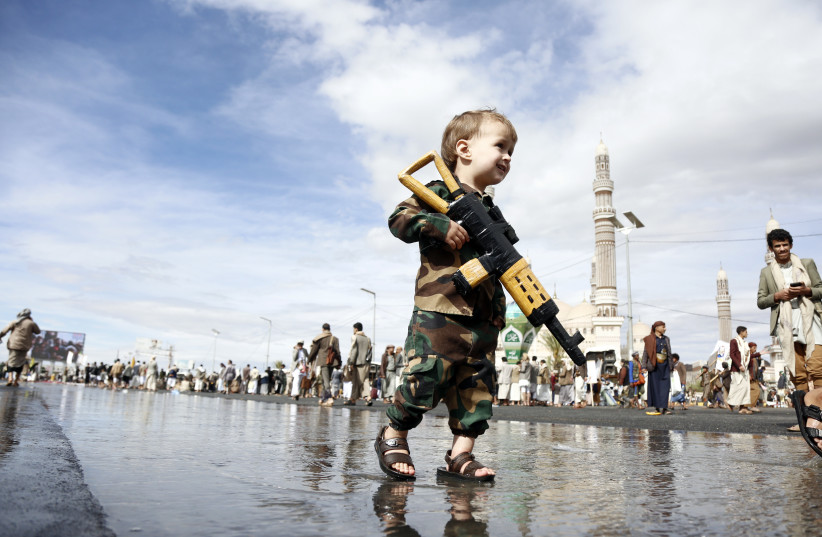 A Yemeni young child dressed in military-style clothing carries a toy rifle while walking through a crowd during a protest staged to show support to Iran against the U.S.-Israel war on March 27, 2026 in Sana'a, Yemen.