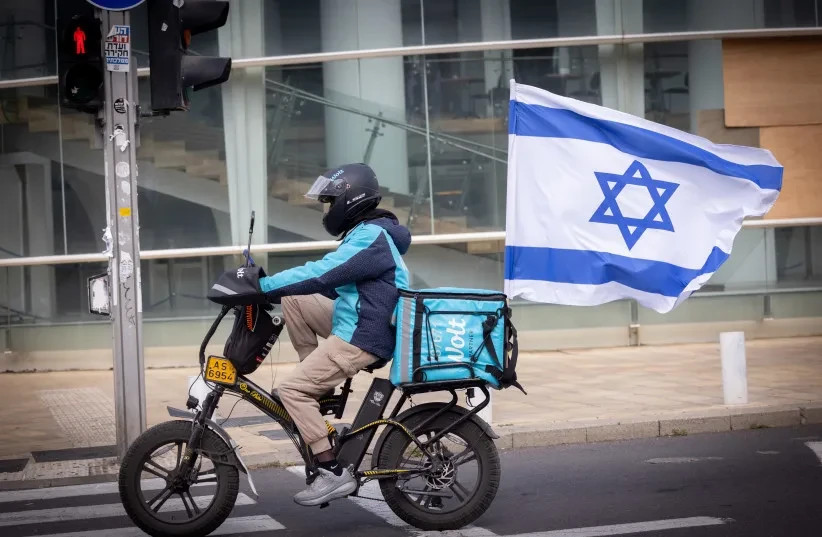Un repartidor de WOLT con una bandera israelí durante la guerra en curso entre Israel-EE. UU. e Irán. 15 de marzo de 2026.  (credit: MIRIAM ALSTER/FLASH90)