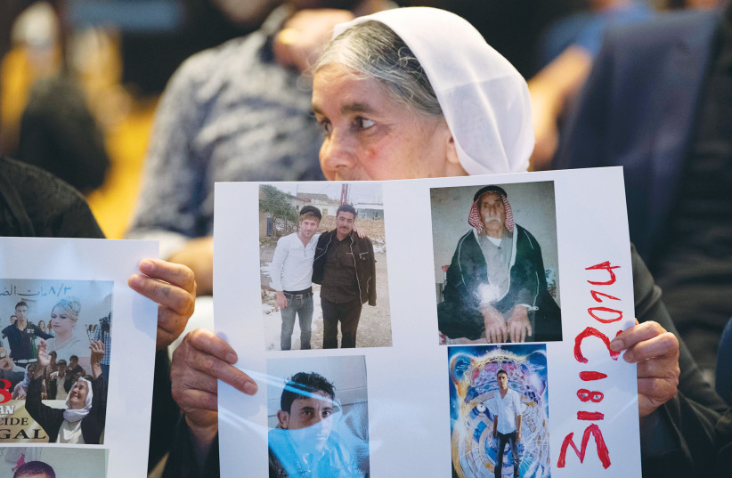 At a commemoration ceremony pertaining to the 2014 ISIS genocide, a Yazidi woman displays photographs of missing relatives in Stuttgart, Germany in 2019. Although Germany has offered safe refuge to thousands of Yazidis, many still carry unanswered questions about murdered or missing relatives.