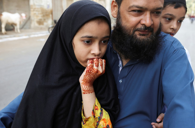 A girl with henna-dyed hands reacts as she, along with her father and brother, watch the slaughter of a sacrificial bull during Eid al-Adha festival in Karachi, Pakistan, May 27, 2026.