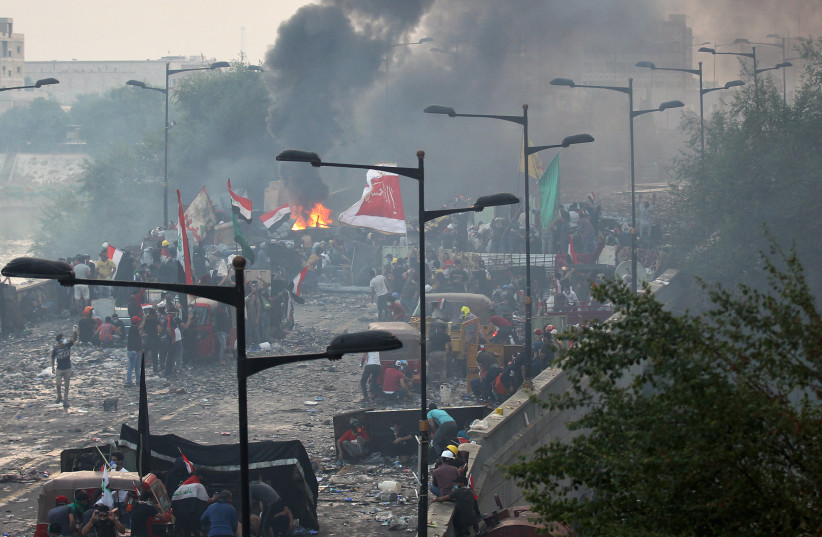 Iraqi anti-government protesters burn debris as they take cover from security forces firing tear gas to keep demonstrators from storming the Green Zone, which hosts government offices and foreign offices, on October 28, 2019 in Baghdad.