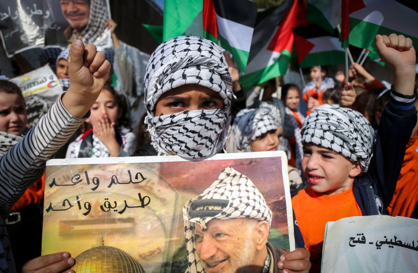 Palestinian children hold placards with a portrait of Yasser Arafat during a rally by Fatah supporters marking the 21th death anniversary of the late former Palestinian president, in the West Bank city of Hebron, November 11, 2025.