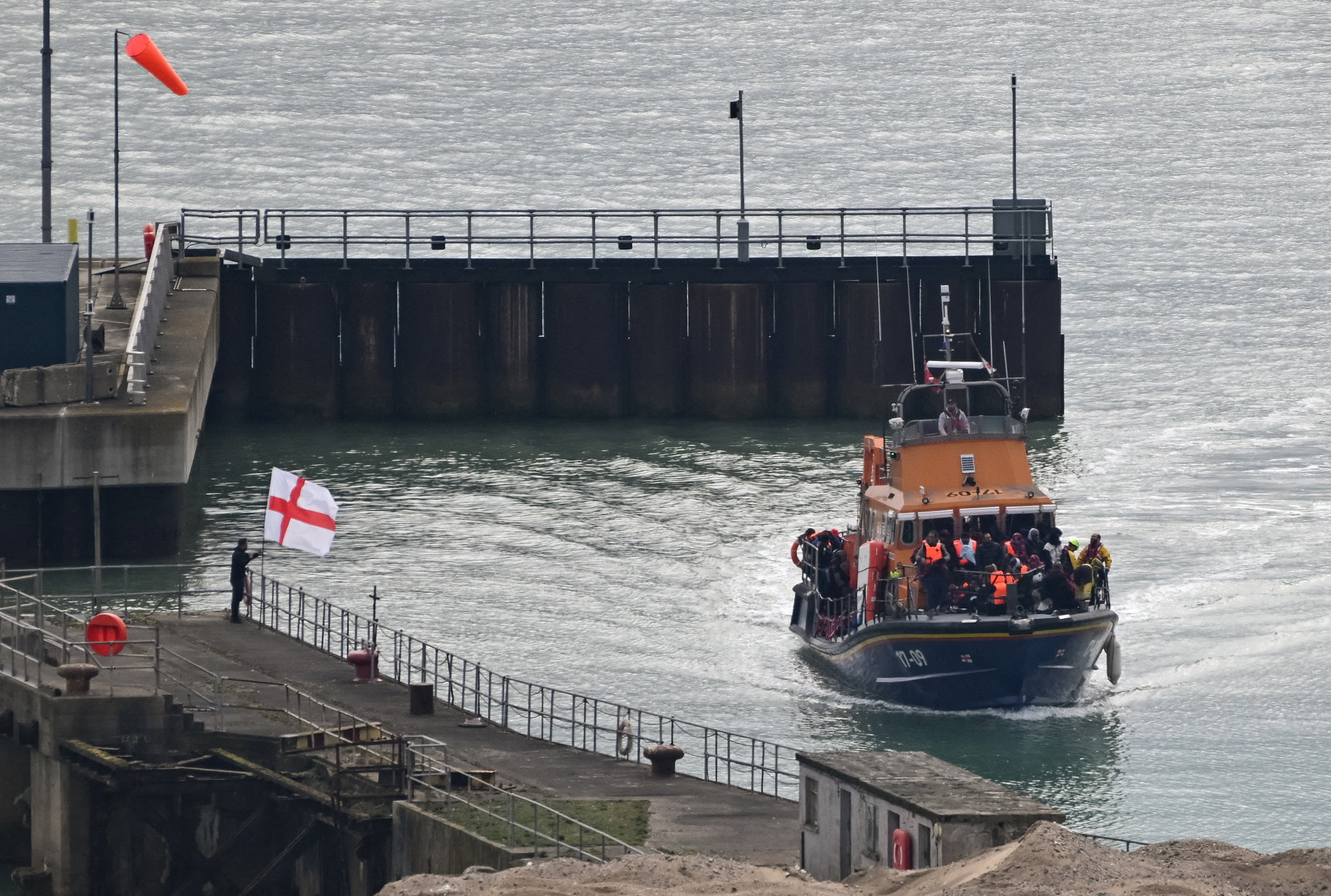 A demonstrator, standing next to an England flag, gestures as a Royal National Lifeboat Institution (RNLI) vessel carrying migrants arrives at the Port of Dover, Britain, April 1, 2026. (photo credit: REUTERS/Chris J. Ratcliffe)