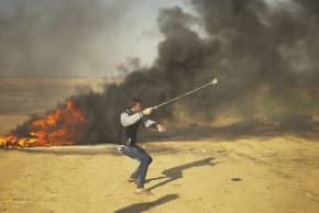 A Palestinian throws a rock towards Israeli forces on the Gaza border