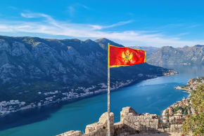 Montenegro flag blowing in the wind with a scenic view from St Ivan fortress on Kotor bay.