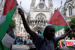 A person holds two Palestinian flags as supporters of the pro-Palestinian campaign group Palestine Action gather outside the High Court in London, Britain, July 4, 2025.