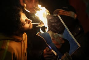 Two men lights a cigarette from a burning picture of Islamic Republic head Ali Khamenei as they set it on fire outside the Iranian embassy in London, UK, at a rally yesterday.