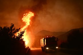  A firetruck drives past flames along a road during a wildfire near the city of Patras, western Greece on August 13, 2025. 