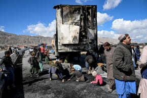 People gather as others collect recyclable items beside a burnt vehicle along a road on the outskirts of Quetta on February 1, 2026 a day after an attack by Baloch separatists. 