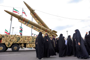 Women walk near ballistic missile launch vehicles in Tehran on February 11, 2026, during a rally marking the 47th anniversary of the 1979 Islamic revolution. 