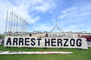 Demonstrators hold a banner that says, "Arrest Herzog" outside Parliament House during a protest against the President of Israel Isaac Herzog’s state visit, in Canberra, Australia, February 11, 2026.