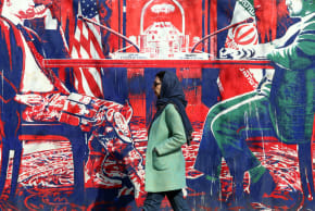 An Iranian woman walk past anti-US mural depicting Iran and US negotiation table, painted on the outer walls of the former US embassy, in Tehran on February 6, 2026.