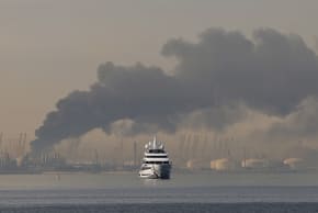 A yacht sails past a plume of smoke rising from the port of Jebel Ali following a reported Iranian strike in Dubai on March 1, 2026. Fresh blasts were heard across the Gulf cities of Dubai, Doha and Manama on Sunday morning after a day of Iran strikes in the region 