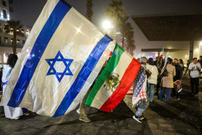 A man draped in a US flag holds stacked Israeli and Royal Iranian flags during a demonstration in solidarity with the Iranian protest movement outside the US Embassy branch office in Tel Aviv on February 14, 2026. 