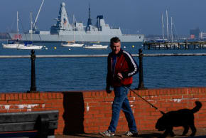 A man walks his dog as the HMS Dragon is undergoing ammunitioning operations at Upper Harbour Ammunitioning Facility (UHAF) in Portsmouth Harbour, March 4, 2026. 