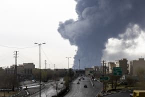 ars drive down a highway as smoke billows after overnight airstrikes on oil depots on March 8, 2026 in Tehran, Iran.