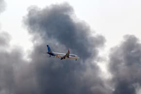 A Flydubai Boeing 737 Max aircraft prepares for landing as a smoke plume rises from an ongoing fire near Dubai International Airport in Dubai on March 16, 2026.