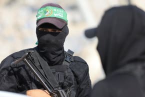 Hamas terrorists look on as they escort members of the Red Cross towards an area within the so-called "yellow line" to which Israeli troops withdrew under the ceasefire in Gaza City November 12, 2025.