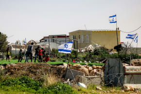 Palestinian boys play football on a pitch surrounded by Israeli flags in the village of Umm al-Kheir, east of Yatta in the south of the West Bank, on February 12, 2026.