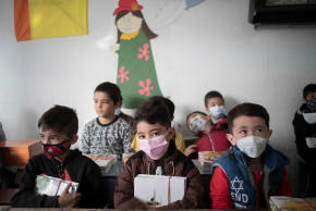 Afghan refugee schoolboys wearing protective face masks look on as they holds their schoolbooks while sitting in a classroom at the Farhang school in the first day of the new academic year in southern Tehran on November 1, 2021.