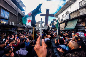 Christian Syrians lift crosses and independence-era flags as they rally in the Duweilaah area of Damascus on December 24, 2024, to protest the burning of a Christmas tree near Hama in central Syria.