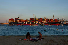 People relax on a beach as the container ship CMA CGM UNITY arrives at Malta Freeport, in Birzebbuga, Malta September 18, 2025.